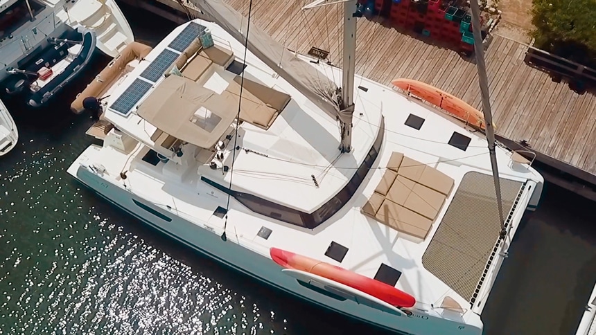 Aerial drone photo of the exterior of Tranquilo, a white Belize catamaran sailboat tied up at a wooden dock.