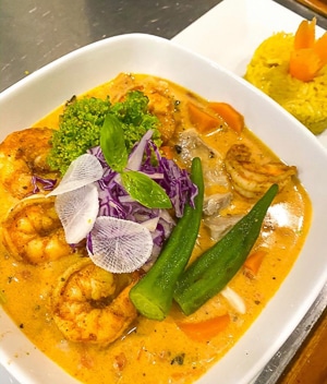 A deeply colored yellow orange shrimp soup topped with green and purple vegetables served in a white bowl served aboard Belize catamaran charter.