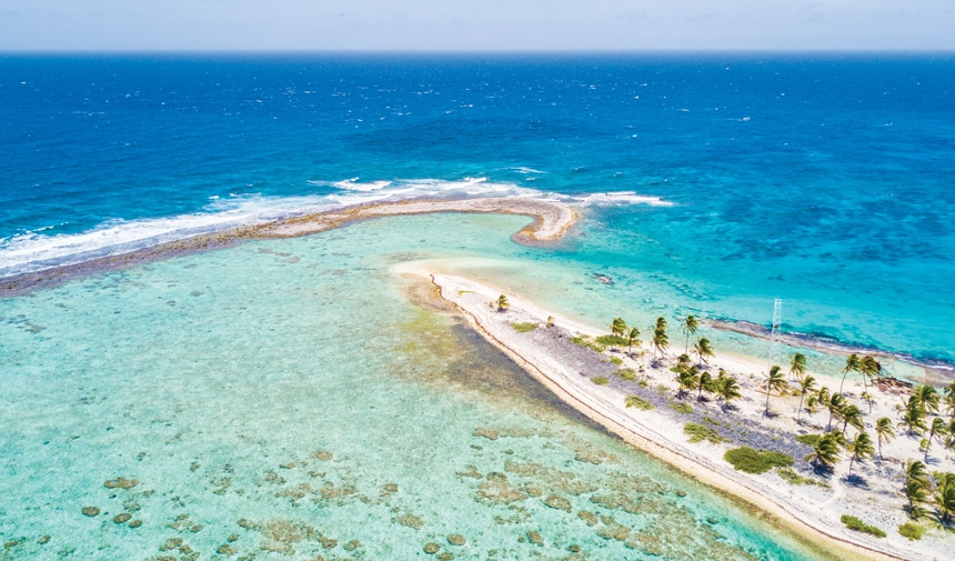 An aerial photo of a Belize caye, a small, low-elevation, sandy island on the surface of a coral reef , stretching out into the crystal teal and blue ocean.