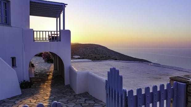 White stucco building with archway and balcony, blue picket fence and cobbled walkway and deck looking out into the ocean.