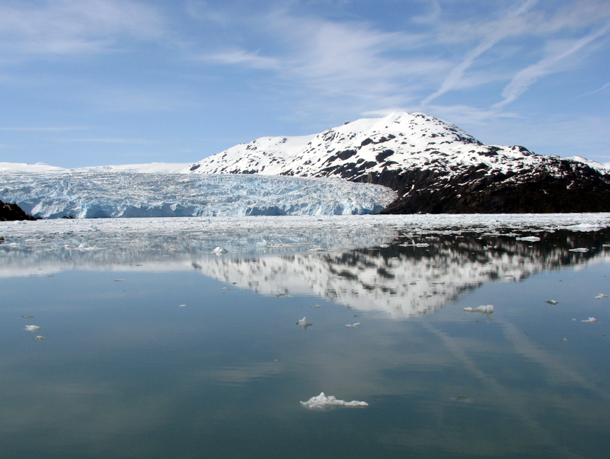 Glaciers relfect in calm waters with snowy mountains.