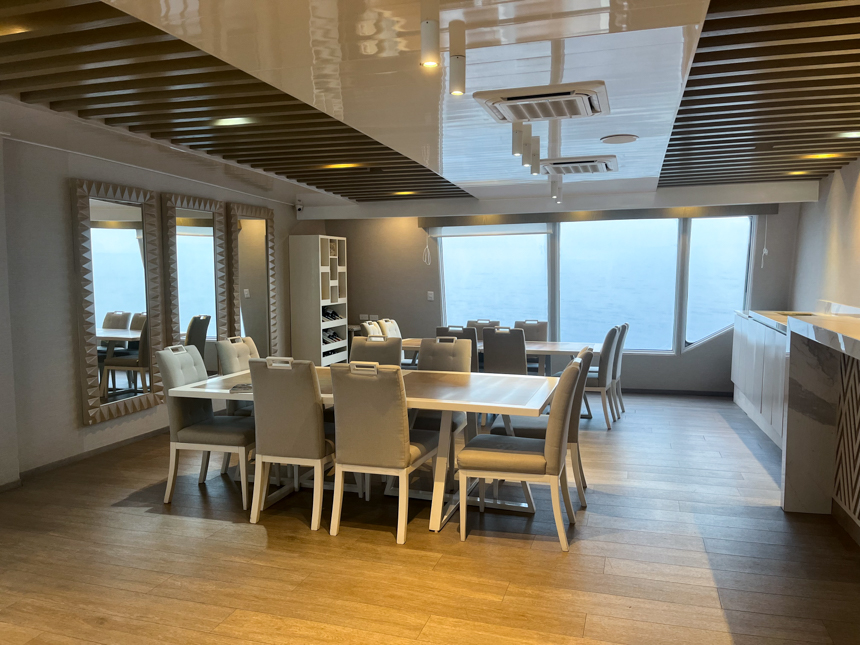The indoor dining room aboard Endemic Galapagos cruise ship, two rectangular tables with grey and white upholstered chairs.