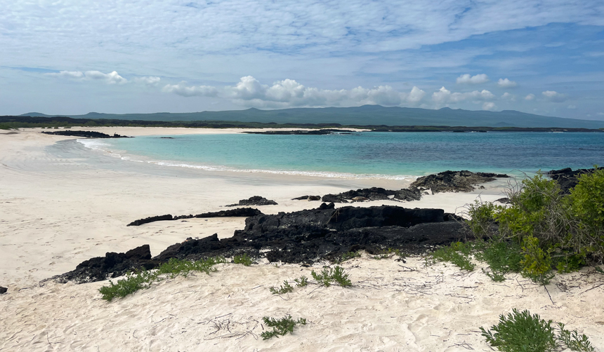 White sand beach of Gardner Bay, crystal teal water with shadowed island in distance,