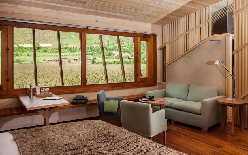Explora Sacred Valley Lodge in Peru suiteroom, with window to corn field, two tables. two chairs a couch and queen bed.