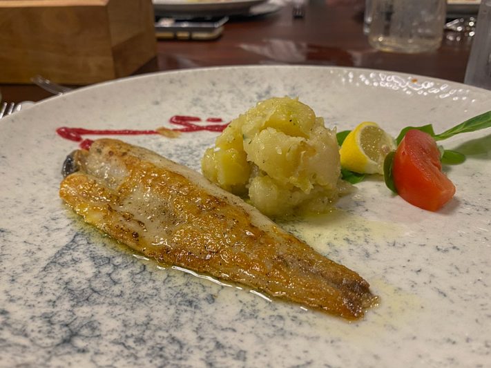 A plate showing a filet of white fish, mashed potatoes, a tomato and lemon slice