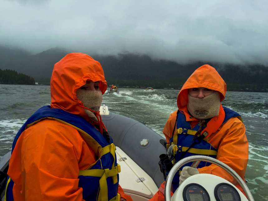 2 people in orange jackets traveling in a zodiac in Alaska.