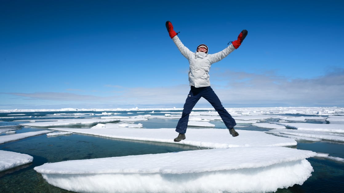 A woman jumping for joy on an ice berg in the Arctic.