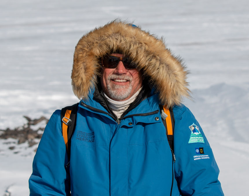 Man in sunglasses & blue parka with fur-lined hood stands atop a snowfield on an Arctic cruise aboard Rembrandt van Rijn.