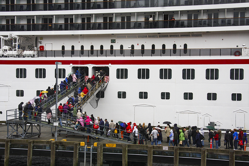 A long line of passengers stand on the dock and boarding stairs to get on a big ship cruise in Alaska