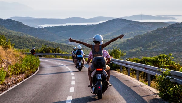 A woman with her arms out on a moped with coastal views in Croatia