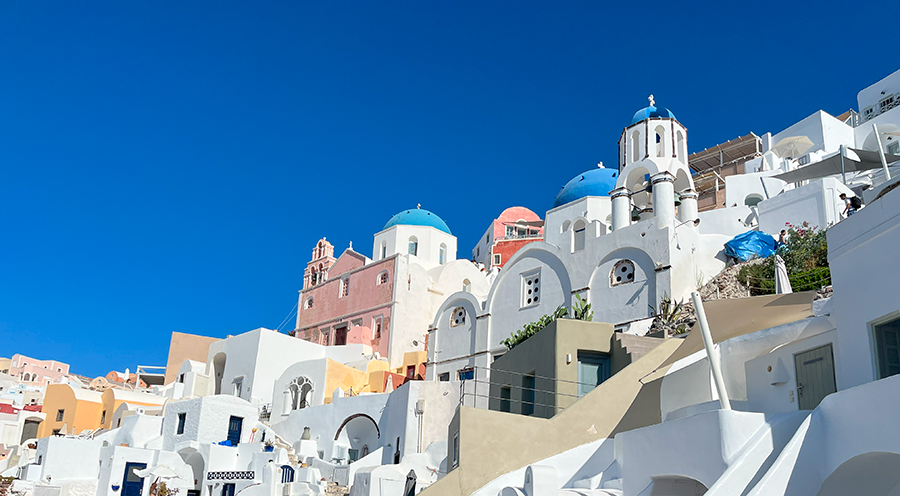 A village with white houses and blue dome roofs with a blue sky. 