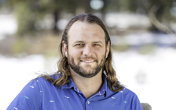A portrait of AdventureSmith specialist Andrew Browning seen smiling with long brown hair and a blue collared shirt