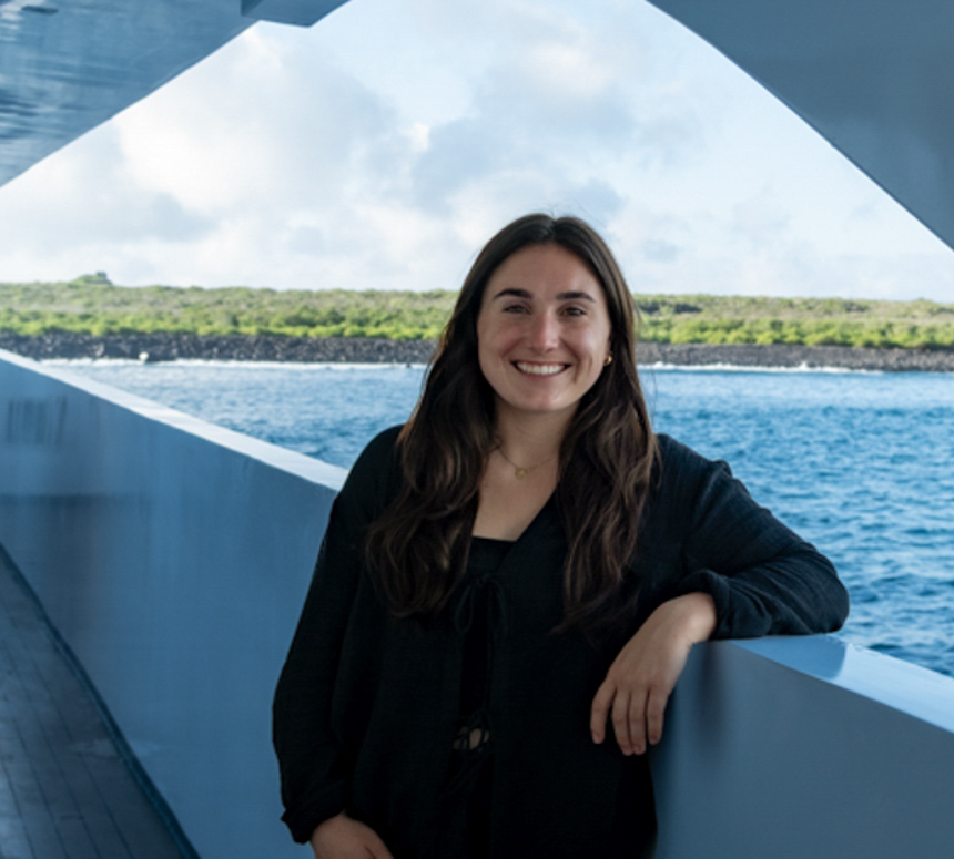 A Galapagos specialist leans on the railing of a ship with mangrove shore behind her