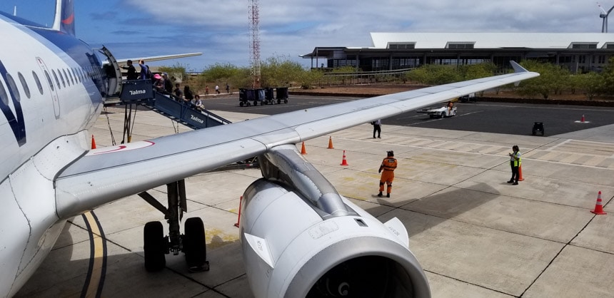 The tin-roofed Baltra Galapagos airport seen from an airplane stairway with the engine and wing in the foreground 