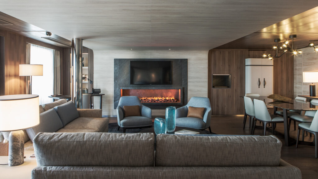 Owner's Suite living room with couch, dining room table, modern light fixtures, wooden interior & wide windows on Le Commandant Charcot.