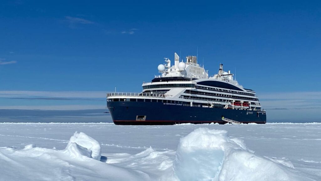 Expedition ship with dark blue hull & white upper decks sits in ice during Le Commandant Charcot Northeast Greenland Voyages.