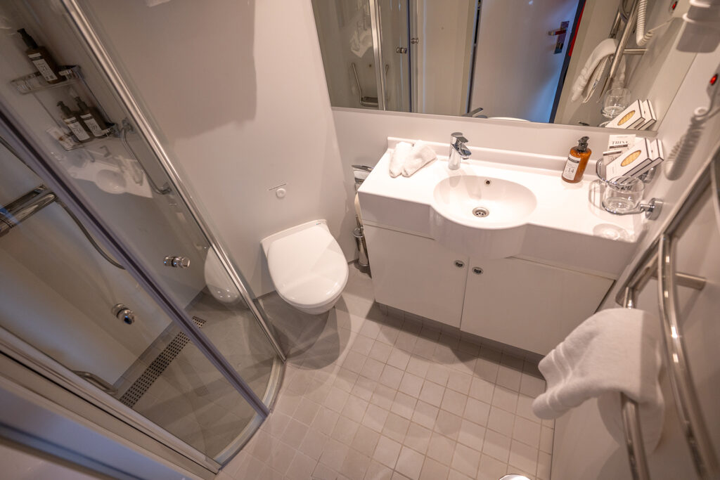 Veranda Cabin bathroom aboard Magellan Explorer. All white with silver appliances. Sink, toilet, shower.