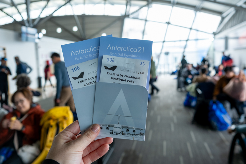 Two tickets for Antarctica21s flight to Antarctica in the airport terminal with travelers off in the distance