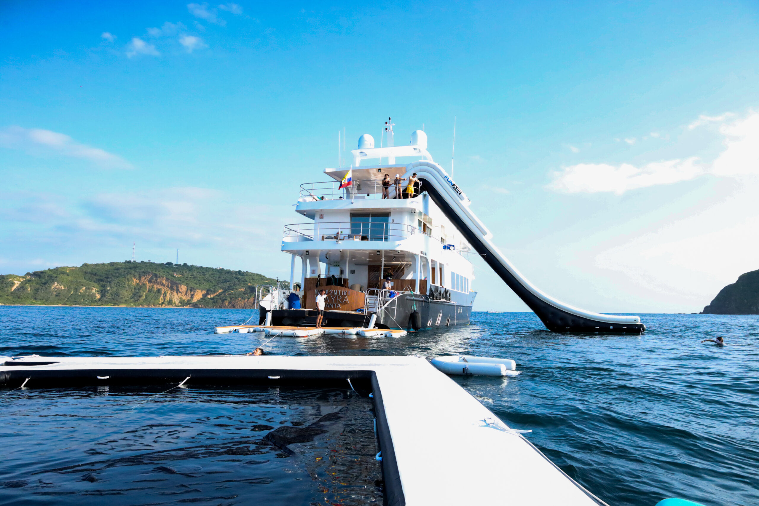 Kontiki Wayra ship anchored in Costa Rica, guests seen swimming around the inflatable slide and harbor and watching from top deck,