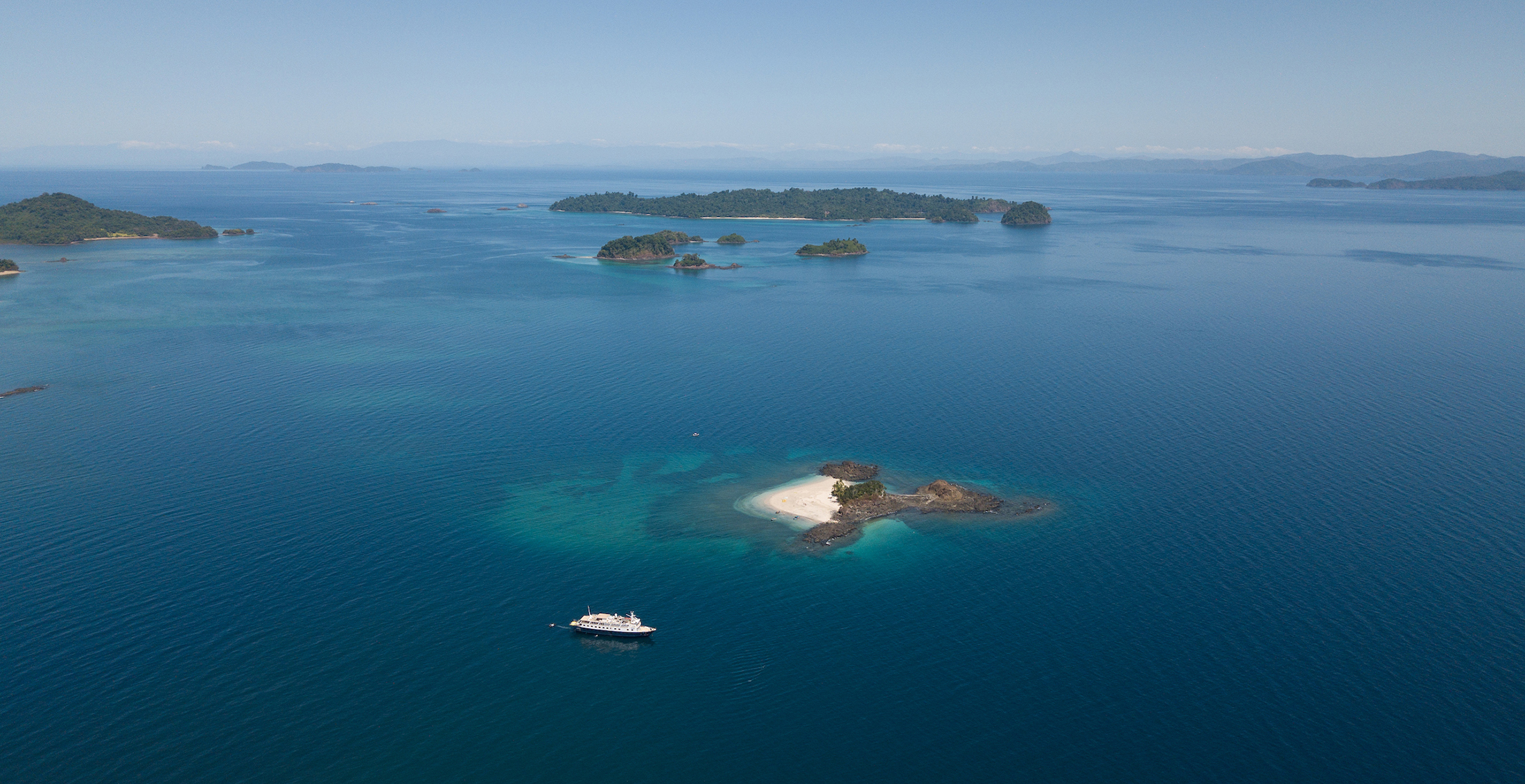 aerial photo of an empty vast blue sea in Costa Rica, dotted with islands, a small white and blue ship is anchored off shore.
