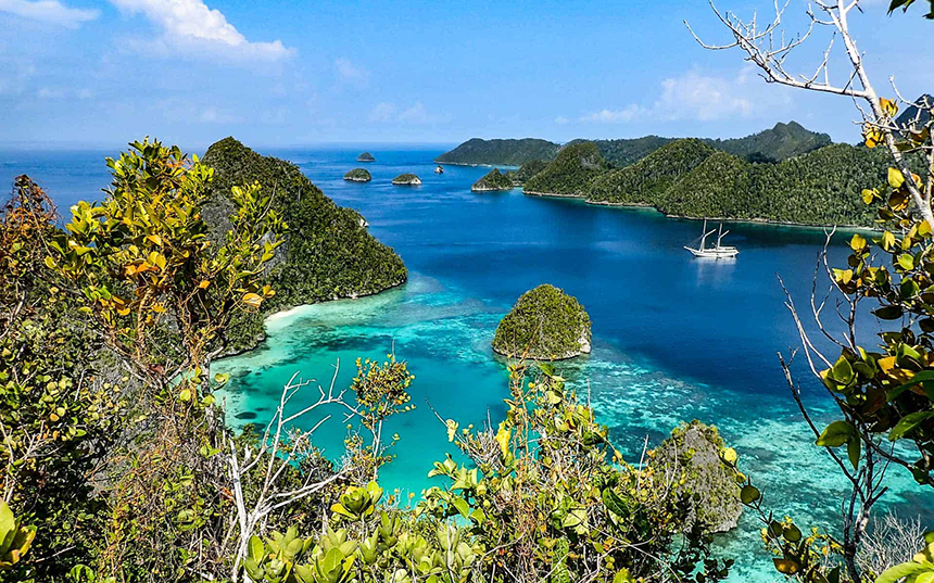 looking down at a beautiful desolate Indonesia cove with a small ship anchored in the middle of it and jungle surrounding it.