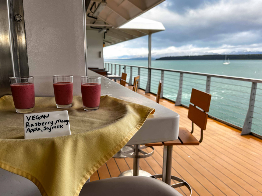 Berry smoothies sit on small tray draped in a yellow cloth on open deck of Nat Geo Venture on a Lindblad Alaska cruise.