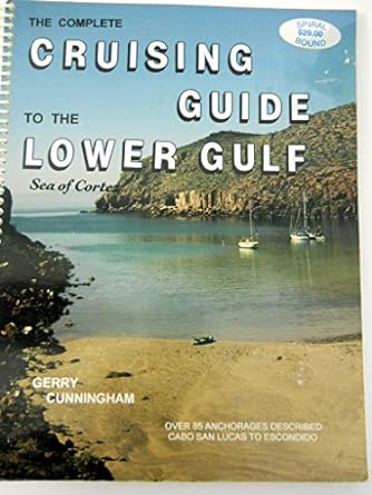 Book cover of the Cruising Guide to the Lower Gulf, Sea of Cortez showing a photograph of a tan beach with two sailboats in a calm cover surrounded by rocky desert landscape and blue sky.