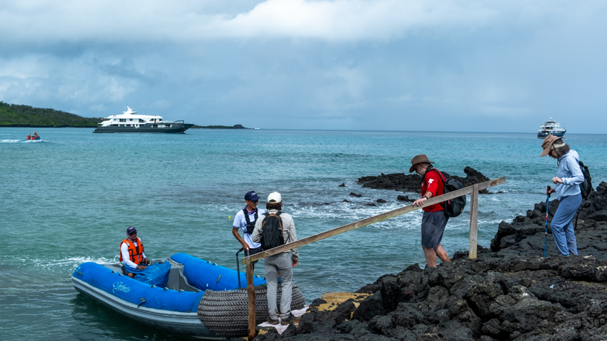 Guests walking on lava rock to  board zodiac to be transferred back to small ship on a cloudy day 