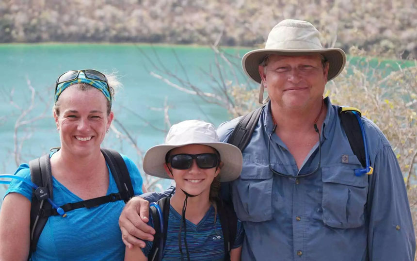 A family of three in blue shirts and hats stands looking at the camera smiling in the Galapagos