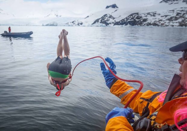 Guest with safety rope attached jumping off a small ship during a polar plunge event in Antarctica.