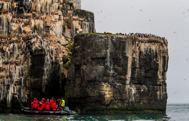 A group of travelers on a skiff in the Arctic waters, in front of a rocky cliffside