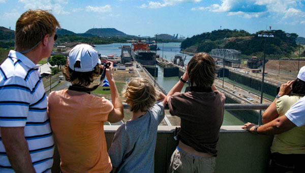 Father & 3 kids overlook a small ship crossing the Miraflores lock in the sun on the best Panama Canal tour.