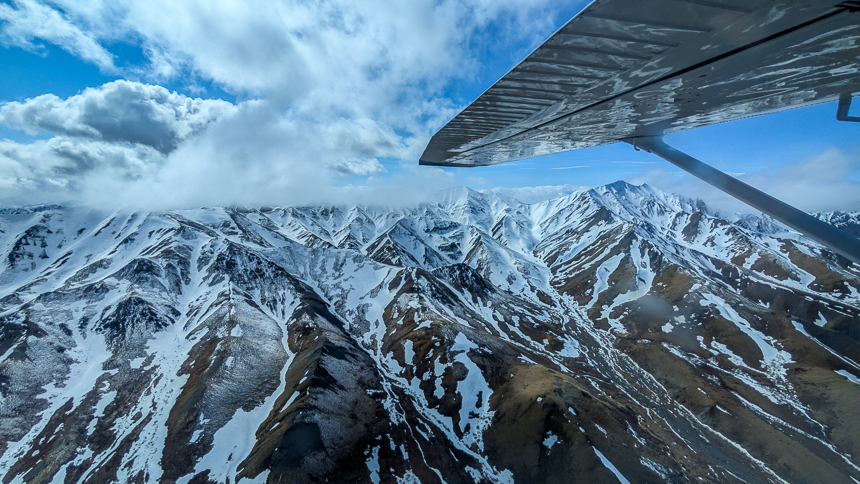 Views from small airplane of snowy mountain ranges on a cloudy day