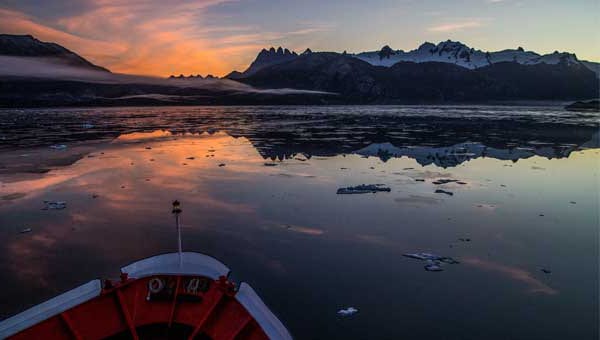 Bow of small expedition ship facing snow-capped peaks at sunset during a Chilean fjords cruise.