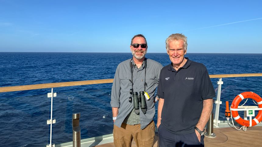 AdventureSmith Exploration Justin and Greg Mortimer standing on deck aboard Douglas Mawson on a bright sunny day with open seas behind them