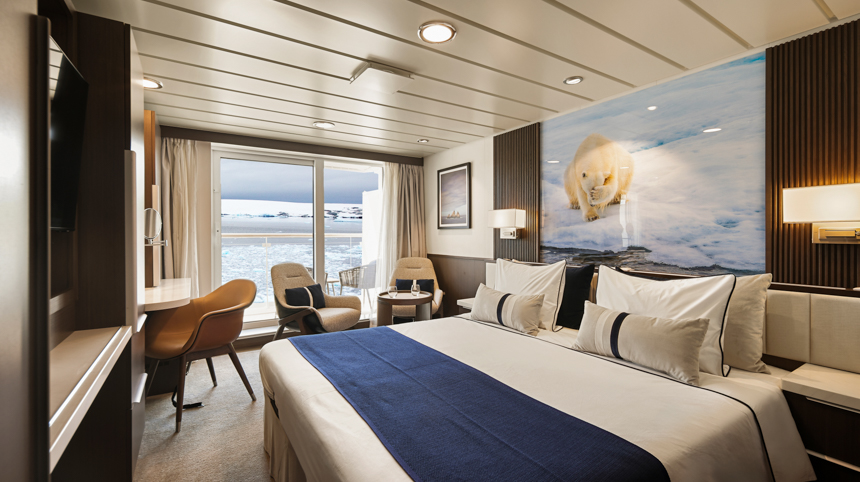 Stateroom aboard Douglas Mawson with large double bed, small seating area and small desk area with large sliding glass doors and polar bear image over the bed 