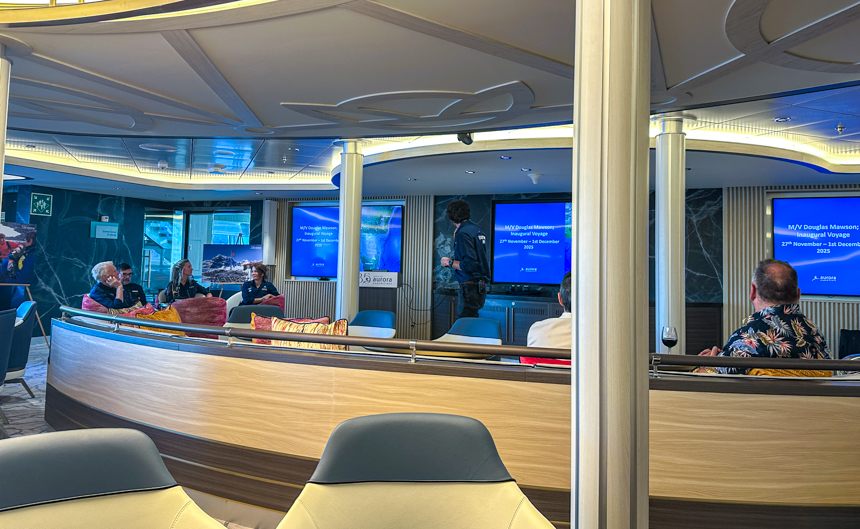 Lecture room with multiple screens and guests sitting and enjoying the informational lecture from expedition guides aboard Douglas Mawson 