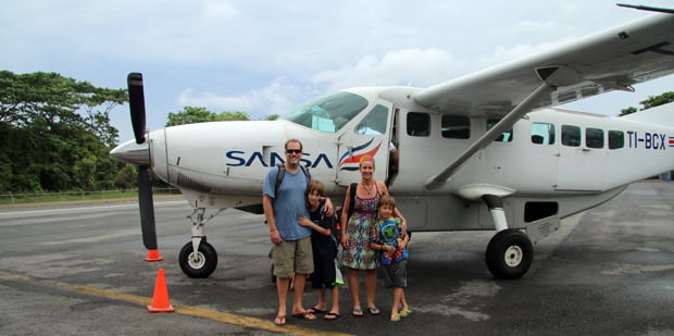 Family travelers (a father, mother and two young sons) standing in front of a plane in Costa Rica