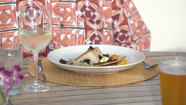 Seared ono fish on a plate with white wine and a Hawaiian Island shirt in the background