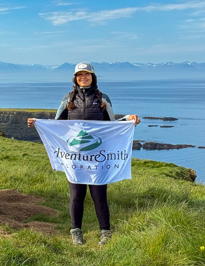 AdventureSmith Specialist standing on the grassy cliffs of Iceland with a white flag in hand, dressed in active adventure clothes