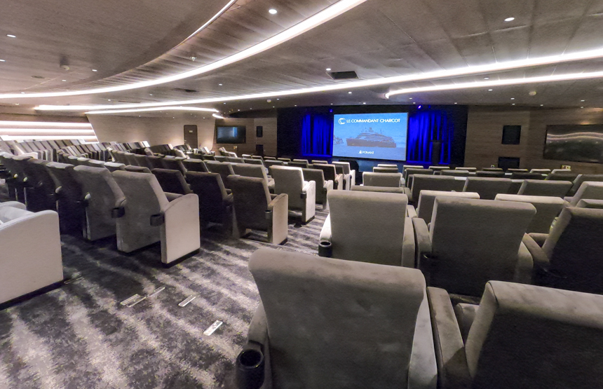 theatre aboard Le Commandant Charcot, grey upholstered movie seats in circular rows around a stage with screen,