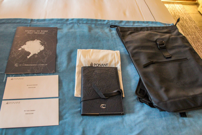 A black waterproof drybag backpack and a leather-bound journal and more Commandant Charcot branded items given to guests.