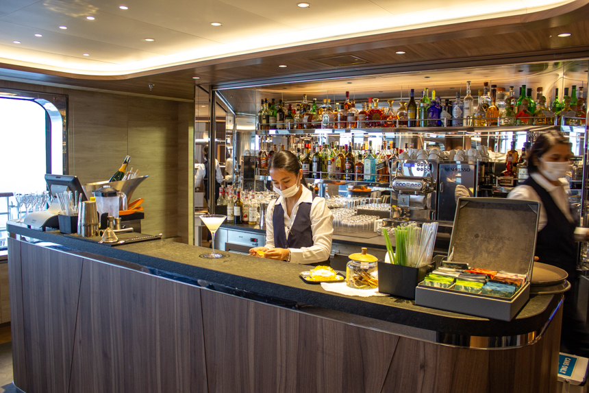Main bar lounge with mirrored glass behind shelves of colorful liquor bottles aboard Le Commandant Charcot ship.