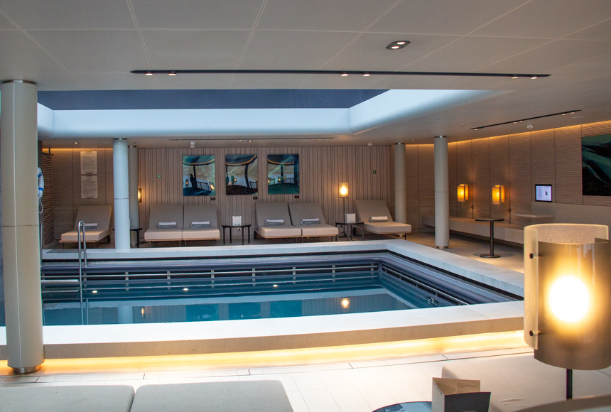 Indoor pool with massive overhead sky light, surrounded by lounge chairs, lamps and artwork by the onboard spa.