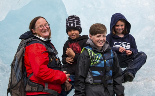 A woman guide in Alaska with a group of smiling kids sitting on an iceberg.