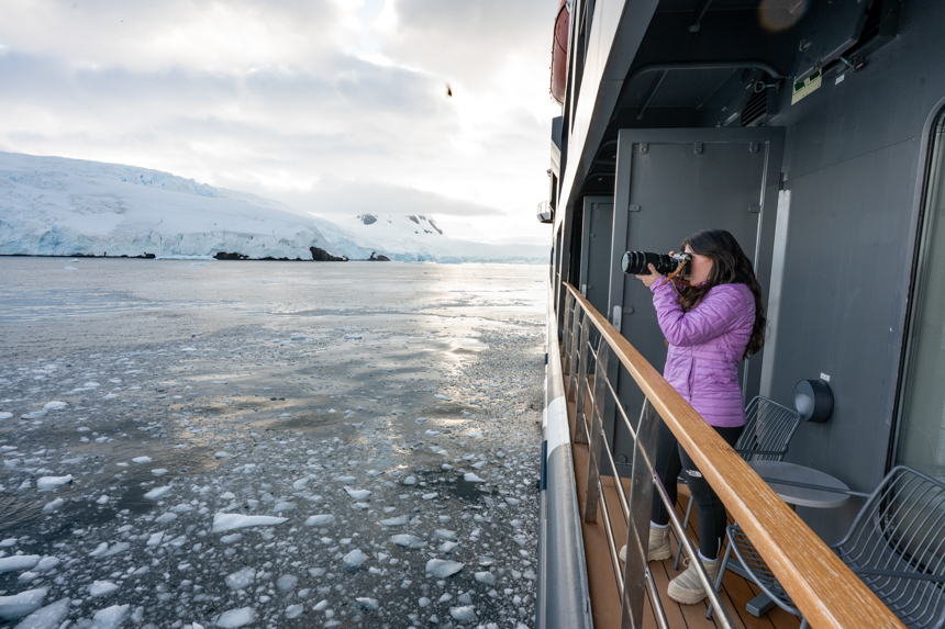 Guest in pink jacket out on the balcony taking photos on Antarctic landscapes