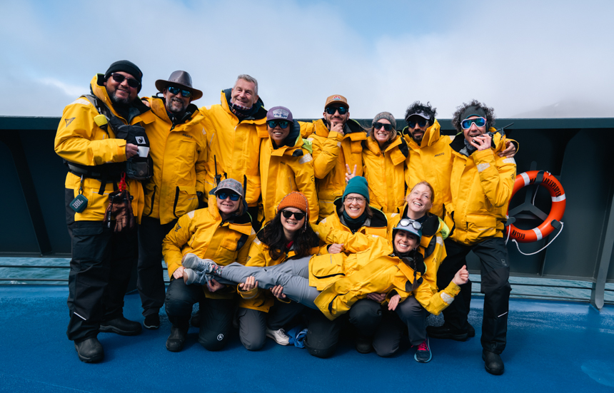 Expedition team dressed in yellow jackets and black pants aboard Magellan Explorer gathered together for a group photo on a sunny day