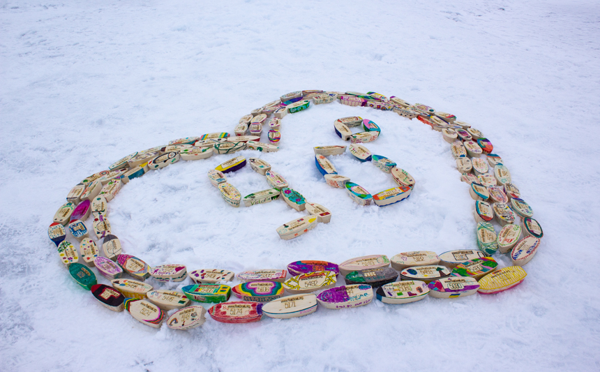 an art piece made of small decorated wooden ships of all colors shaped in a heart around 90 degree symbol