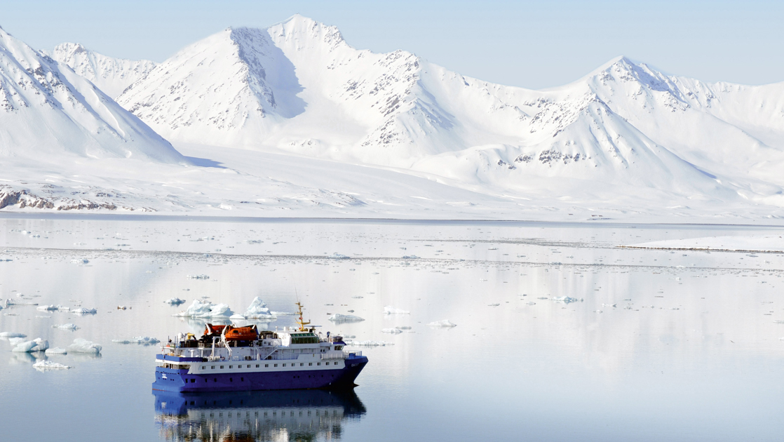 Small cruise ship cruising through the icy waters in front of breathtaking white mountains. 