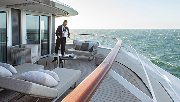 Server in formal wear & white gloves delivers a chilled bottle of champagne to an empty deluxe suite terrace of Le Jacques Cartier French ship as she sails in open waters.